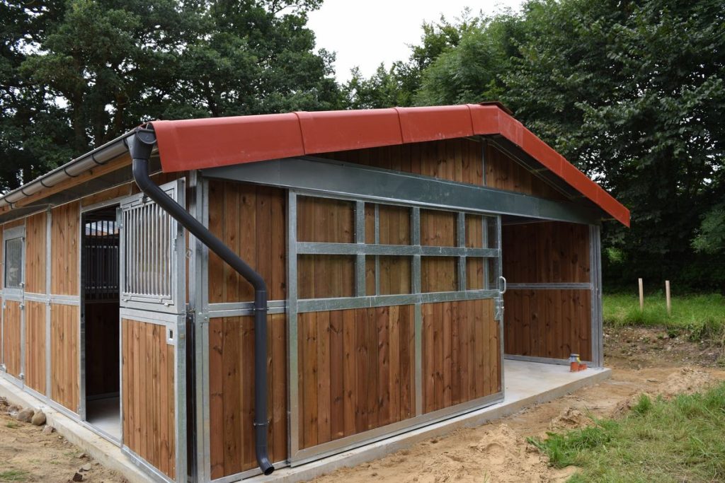 Zweireihiger Stall mit brauner Dachrinne und rotem Dach.